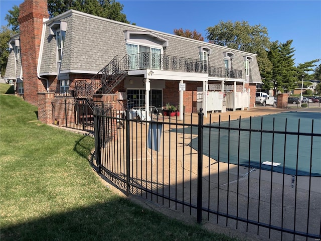 rear view of property with a balcony, a covered pool, and a yard