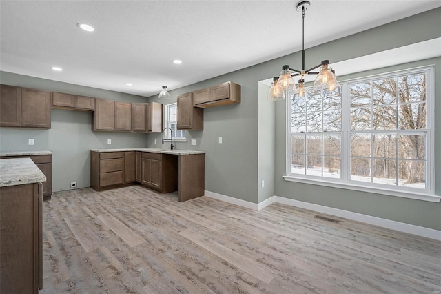 kitchen with sink, light hardwood / wood-style flooring, hanging light fixtures, light stone counters, and a chandelier