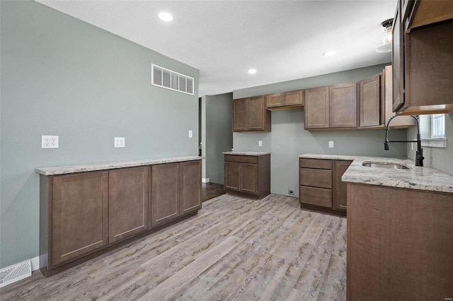 kitchen with a sink, visible vents, light stone countertops, and light wood-style flooring