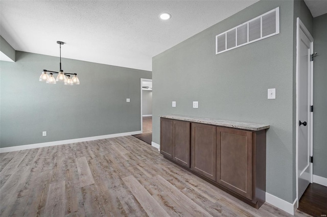 empty room with light wood-type flooring, an inviting chandelier, and a textured ceiling