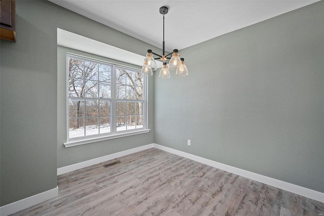 empty room with an inviting chandelier, wood finished floors, visible vents, and baseboards