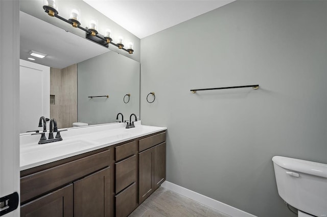 bathroom featuring a sink, baseboards, toilet, and double vanity