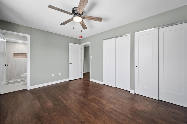 unfurnished bedroom with multiple closets, a ceiling fan, ensuite bathroom, wood finished floors, and baseboards