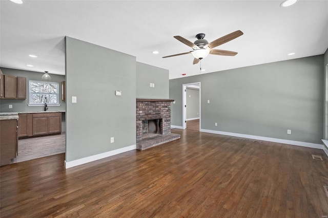 unfurnished living room with ceiling fan, dark hardwood / wood-style flooring, sink, and a brick fireplace