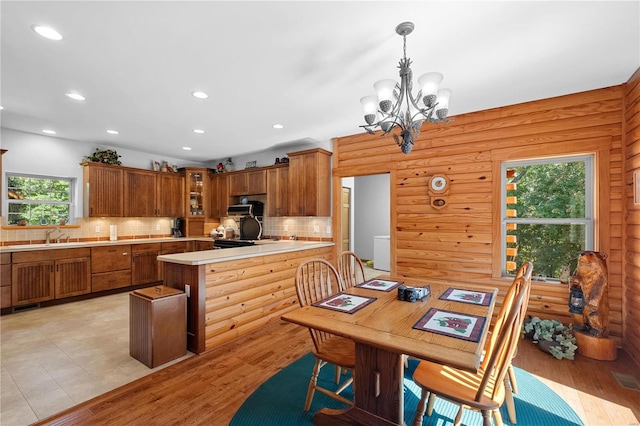 kitchen featuring a chandelier, light hardwood / wood-style flooring, wooden walls, decorative backsplash, and hanging light fixtures