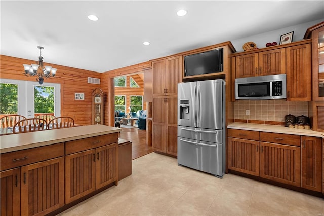 kitchen featuring wooden walls, decorative backsplash, stainless steel appliances, pendant lighting, and a notable chandelier