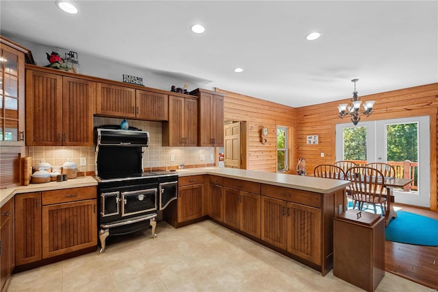 kitchen featuring pendant lighting, wood walls, kitchen peninsula, tasteful backsplash, and a chandelier