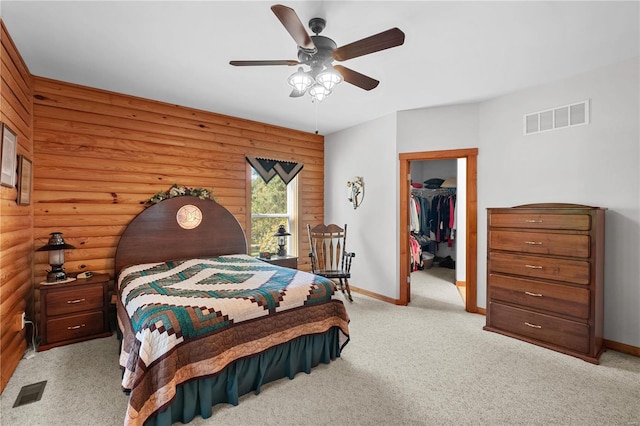 bedroom featuring ceiling fan, rustic walls, a walk in closet, a closet, and light colored carpet