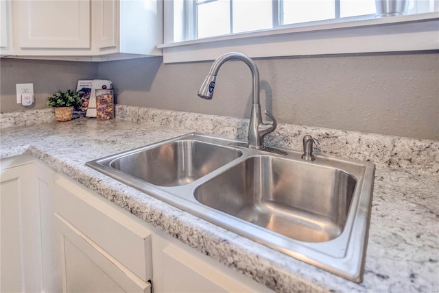 details with white cabinets, light stone countertops, and sink