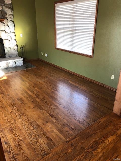 unfurnished living room with dark wood-type flooring and a stone fireplace