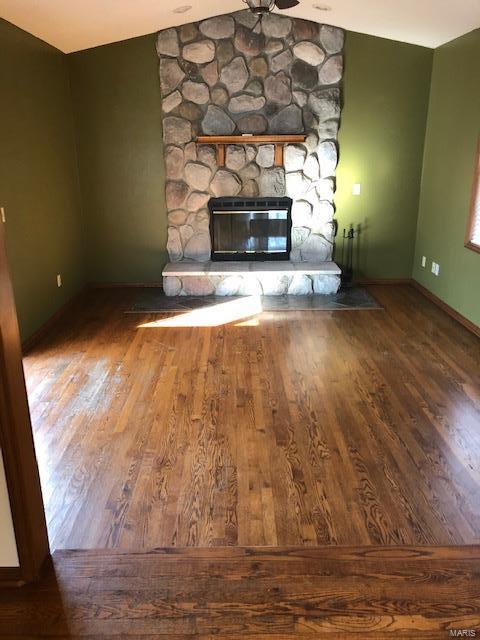 unfurnished living room featuring lofted ceiling, a stone fireplace, and wood-type flooring