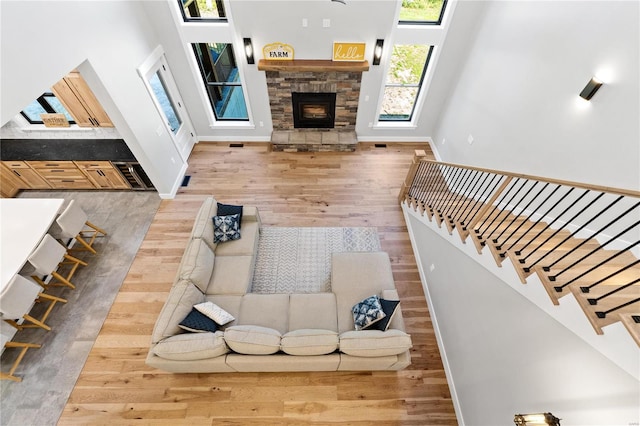 living room with a high ceiling, a stone fireplace, and hardwood / wood-style floors