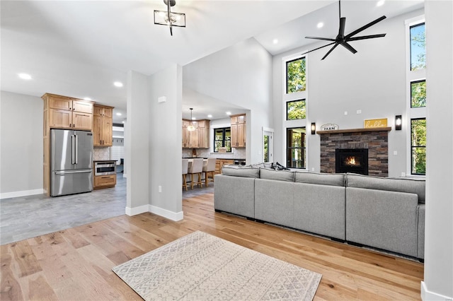 living room with a high ceiling, light wood-type flooring, ceiling fan, and a stone fireplace