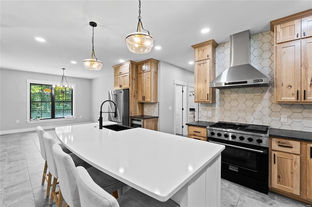 kitchen featuring an island with sink, stainless steel appliances, wall chimney range hood, hanging light fixtures, and backsplash