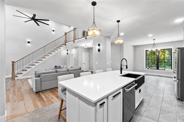 kitchen with sink, white cabinetry, light hardwood / wood-style flooring, a center island with sink, and decorative light fixtures