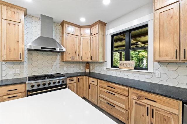 kitchen featuring high end range, wall chimney range hood, dark stone counters, and tasteful backsplash