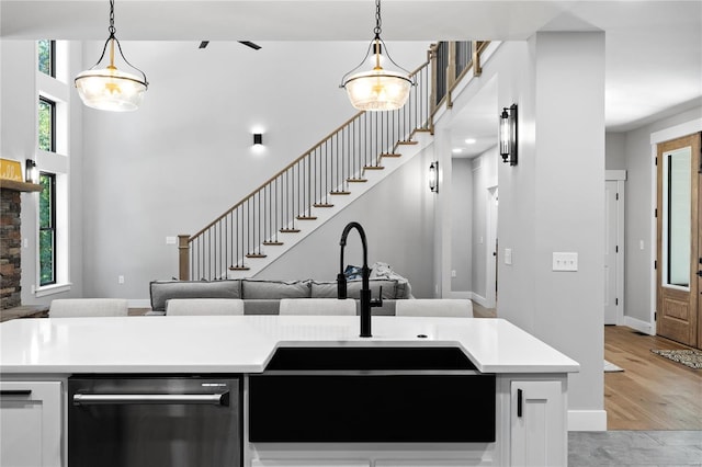 kitchen with light hardwood / wood-style flooring, hanging light fixtures, sink, and stainless steel dishwasher