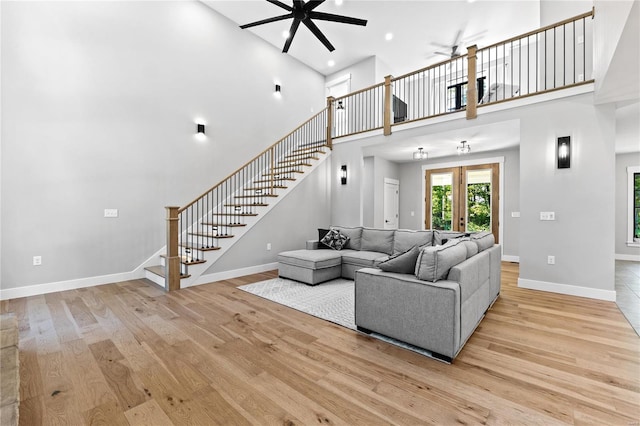 living room featuring light wood-type flooring, ceiling fan, a towering ceiling, and french doors