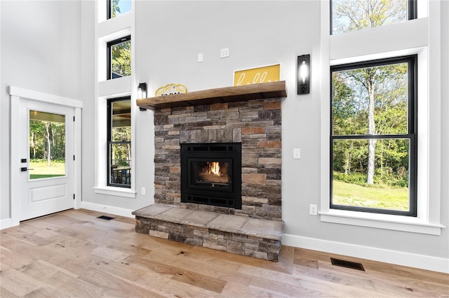 unfurnished living room featuring a towering ceiling, plenty of natural light, light hardwood / wood-style floors, and a stone fireplace