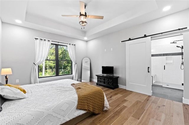 bedroom featuring a tray ceiling, ceiling fan, a barn door, and hardwood / wood-style floors