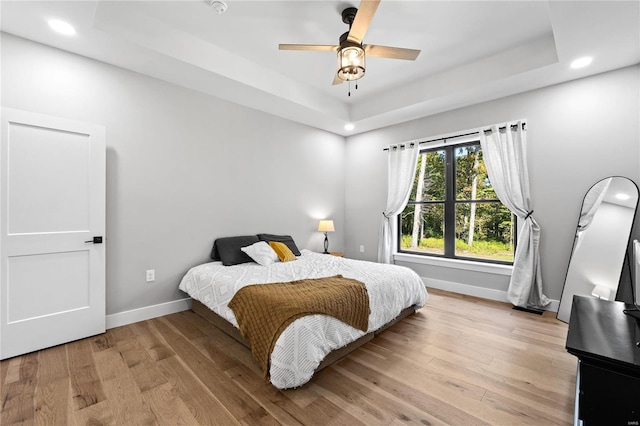 bedroom featuring a raised ceiling, light hardwood / wood-style flooring, and ceiling fan