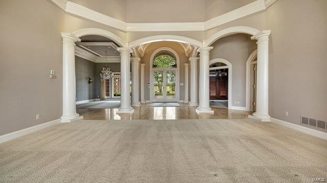 interior space with a towering ceiling, ornamental molding, decorative columns, and light carpet