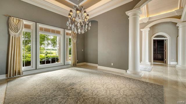 unfurnished room featuring ornamental molding, ornate columns, tile patterned flooring, and an inviting chandelier