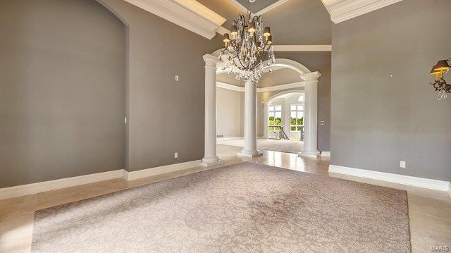 empty room featuring ornate columns, ornamental molding, a notable chandelier, and vaulted ceiling