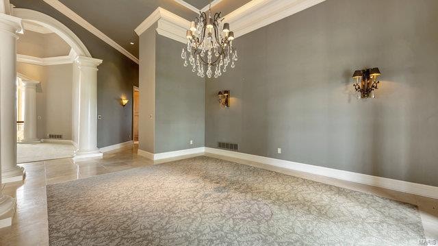 spare room with ornate columns, ornamental molding, a notable chandelier, and a towering ceiling