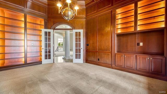 unfurnished room with wood walls, built in shelves, an inviting chandelier, carpet, and french doors