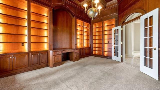 unfurnished office featuring built in shelves, french doors, wooden walls, built in desk, and light colored carpet