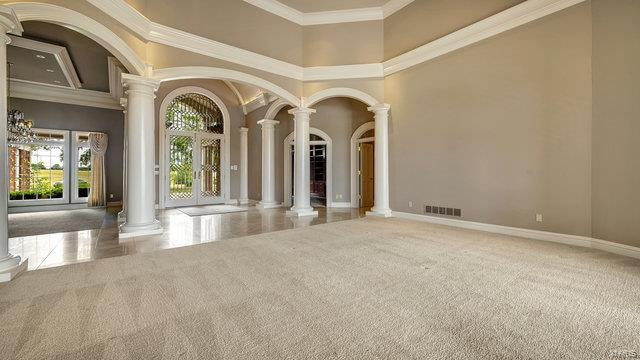 carpeted empty room with ornate columns, crown molding, a high ceiling, and a notable chandelier