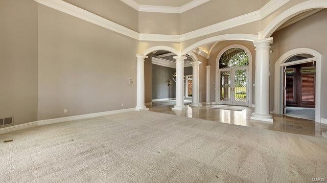 unfurnished room featuring crown molding, decorative columns, carpet, and a high ceiling