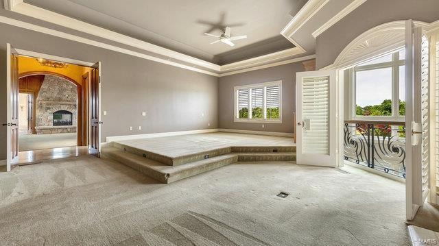 carpeted spare room with ceiling fan, a tray ceiling, a fireplace, and crown molding