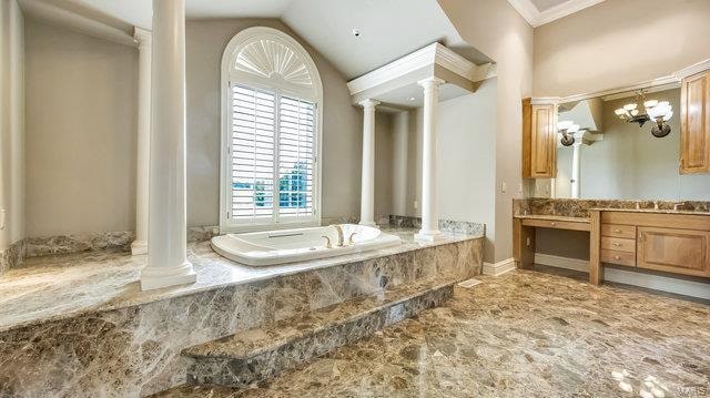 bathroom with ornate columns, vaulted ceiling, ornamental molding, a relaxing tiled tub, and vanity