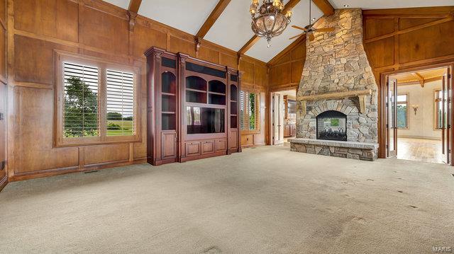 unfurnished living room featuring wood walls, carpet floors, beam ceiling, a fireplace, and high vaulted ceiling