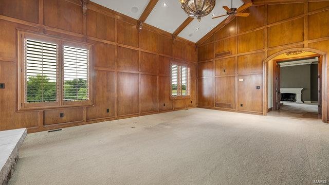 empty room with light carpet, wood walls, and ceiling fan