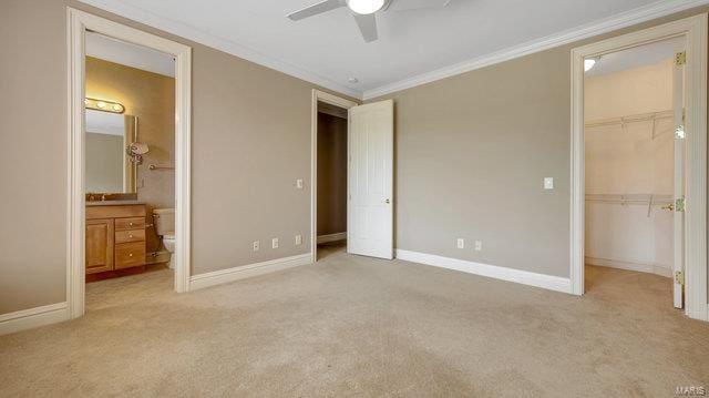 unfurnished bedroom with ceiling fan, light colored carpet, ensuite bathroom, and a spacious closet