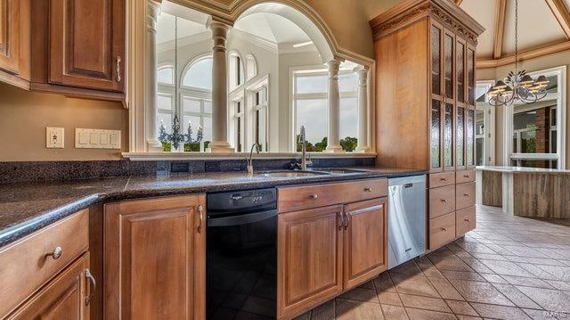 kitchen featuring ornamental molding, decorative columns, dark stone countertops, and dishwasher