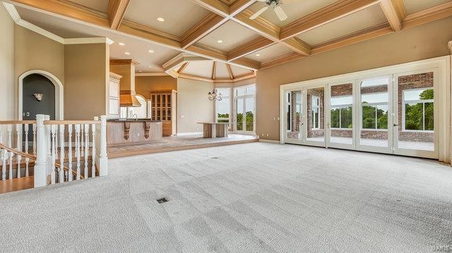 carpeted spare room featuring ceiling fan with notable chandelier, plenty of natural light, ornamental molding, and coffered ceiling