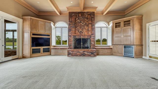 unfurnished living room featuring a brick fireplace, ornamental molding, light colored carpet, and beamed ceiling