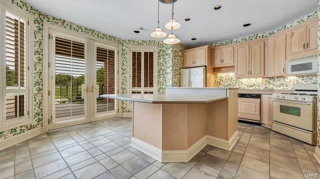 kitchen featuring light brown cabinetry, hanging light fixtures, and white appliances