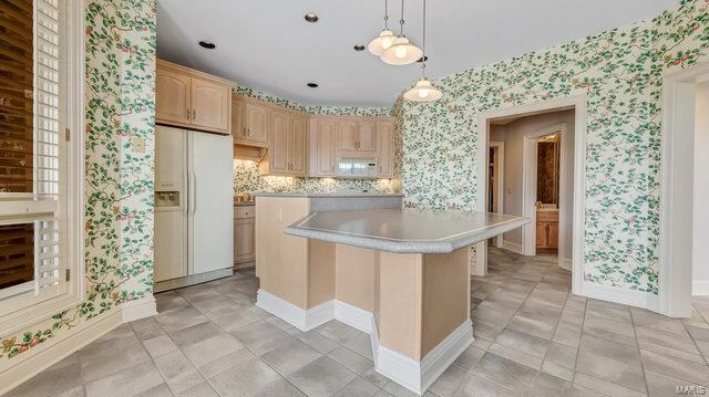 kitchen featuring a kitchen island, white appliances, hanging light fixtures, light brown cabinetry, and a kitchen bar