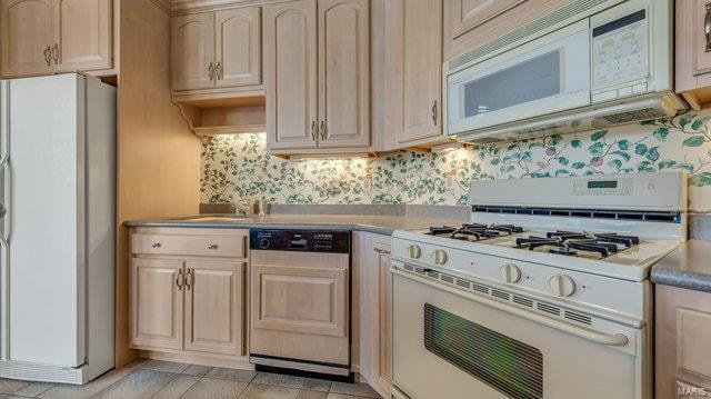 kitchen with light brown cabinets, light tile patterned floors, white appliances, and decorative backsplash