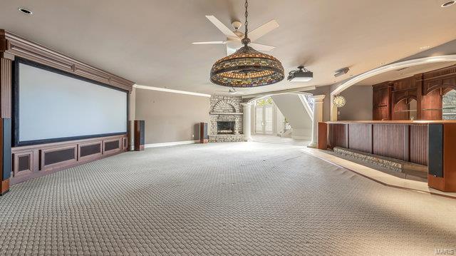 cinema with ornate columns, ceiling fan, a stone fireplace, and carpet