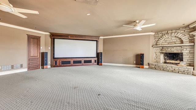 cinema room with ceiling fan, a stone fireplace, crown molding, and carpet flooring