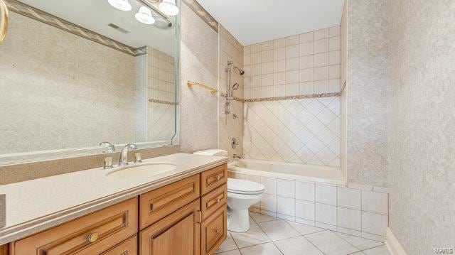 full bathroom with tile patterned flooring, tiled shower / bath, vanity, and toilet