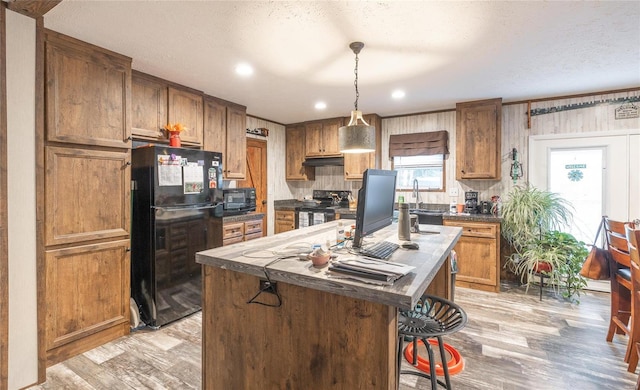 kitchen with light wood-type flooring, black appliances, a center island, decorative light fixtures, and a kitchen breakfast bar