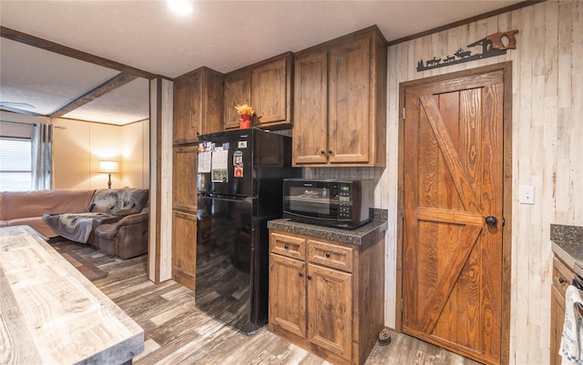 kitchen featuring a textured ceiling, wooden walls, black refrigerator, and light hardwood / wood-style flooring