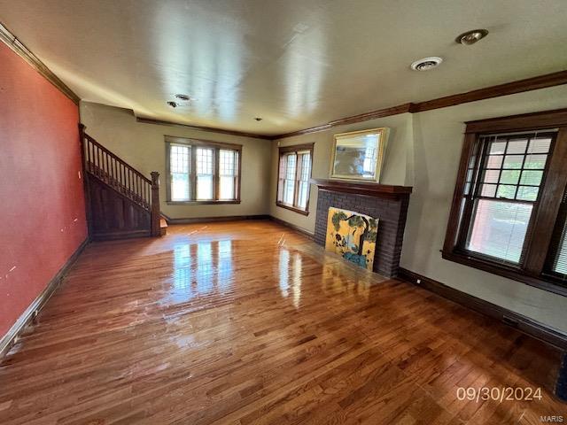 unfurnished living room with wood-type flooring, a tiled fireplace, and ornamental molding